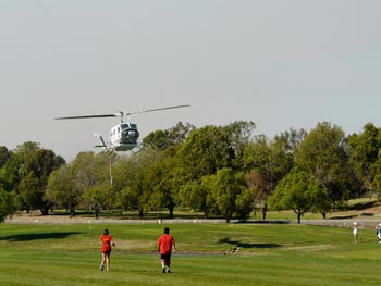 Water dropping helicopter dips low over golf course.